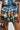 Someone is dressed in the OVERRATED PLAID MINI SKIRT, featuring a layered design with multicolored plaid and a denim trim waistband. The high-rise mini skirt showcases blue, brown, and beige tones and is paired with a matching cropped top. They are holding a brown handbag.