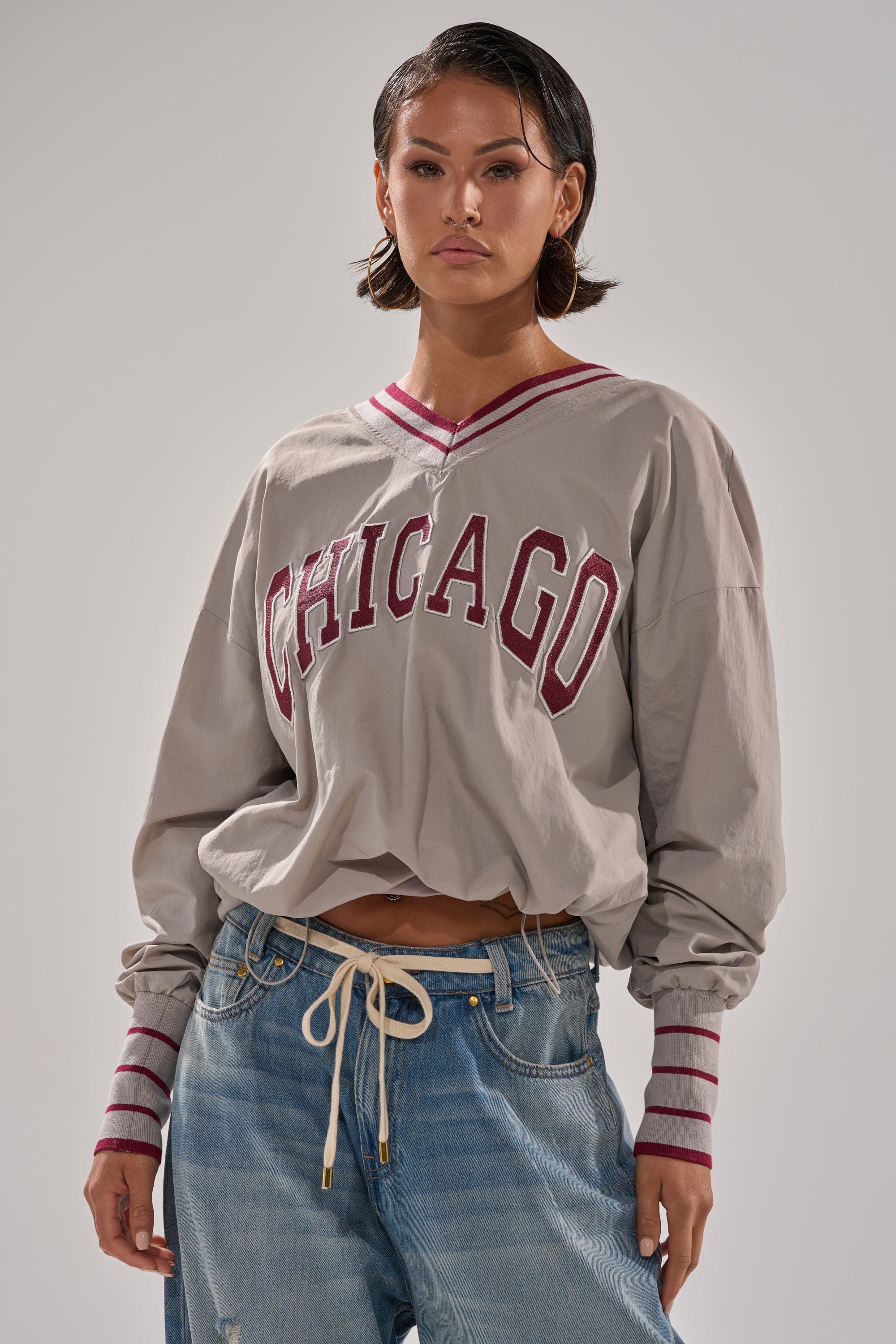 Someone models the CHICAGO V-NECK SWEATSHIRT with red trim and light blue drawstring jeans, standing facing forward against a plain background.