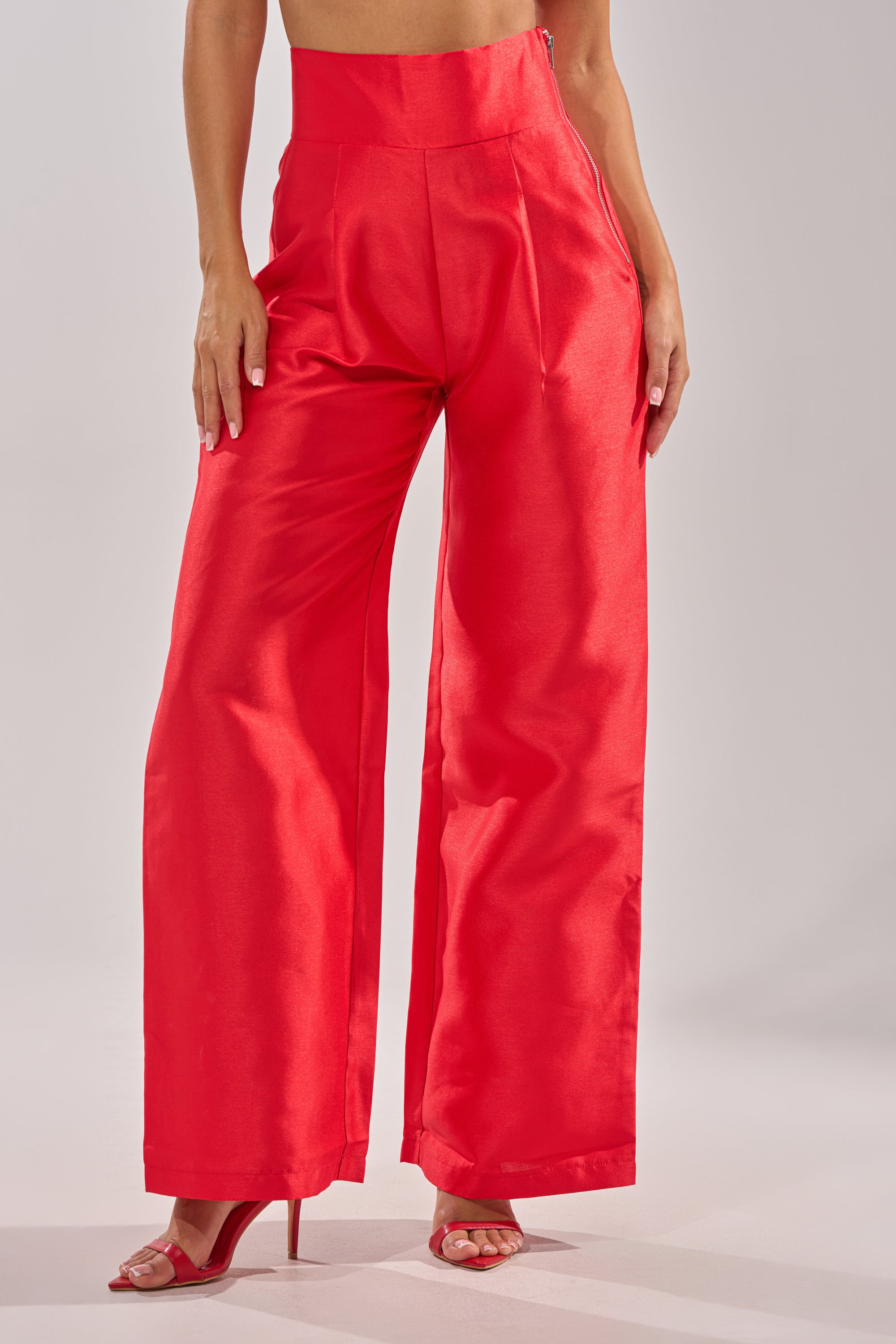 Wearing the BY MY SIDE TROUSER—flowy, high-rise wide-leg red satin pants—with matching red heeled sandals, a person stands against a plain light background. Only their lower half is visible. 1