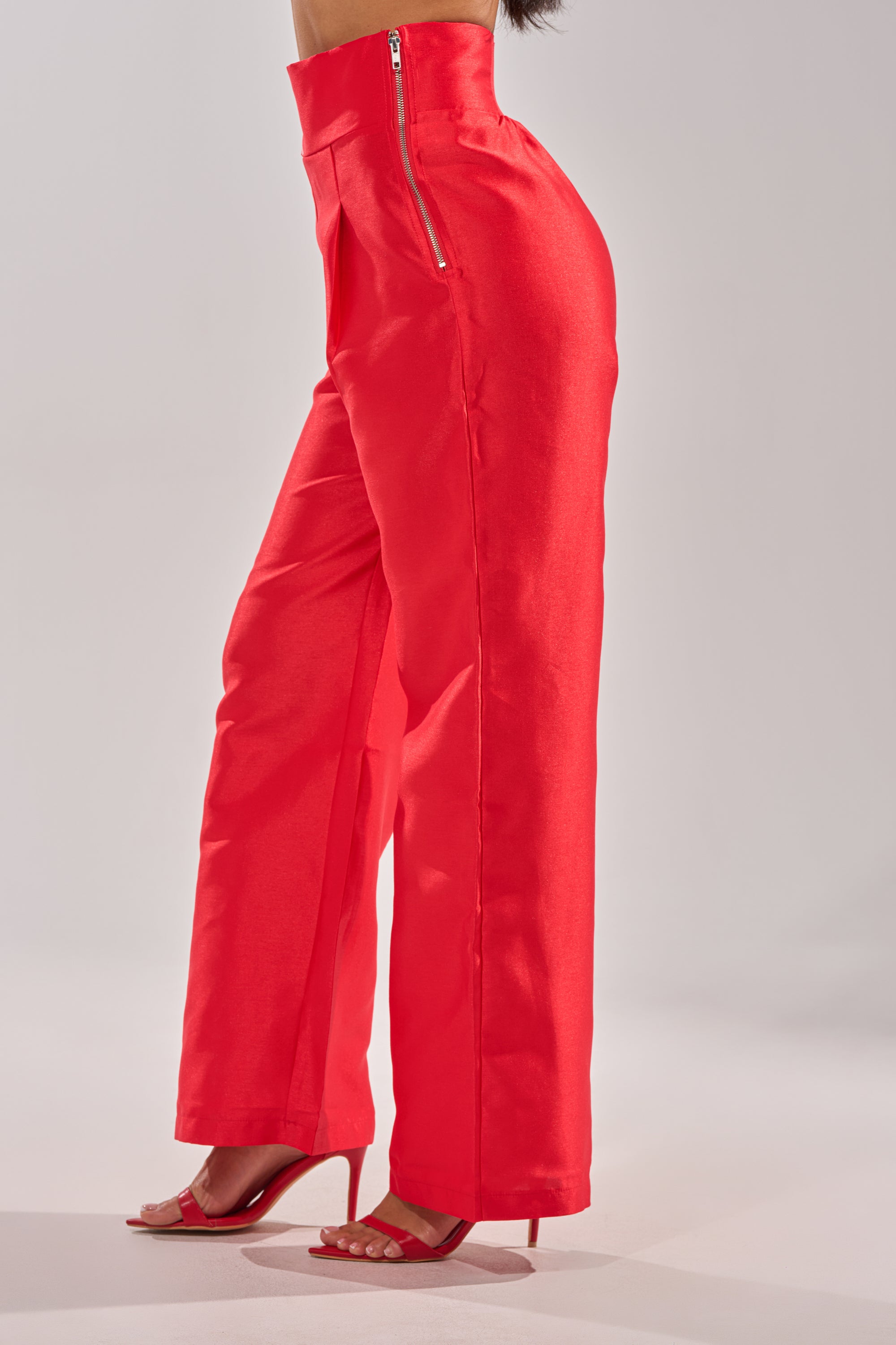 A person models the BY MY SIDE TROUSER—high-rise, wide-leg, bright red pants with a side zipper and matching heeled sandals—shown from the side against a plain light background. 2