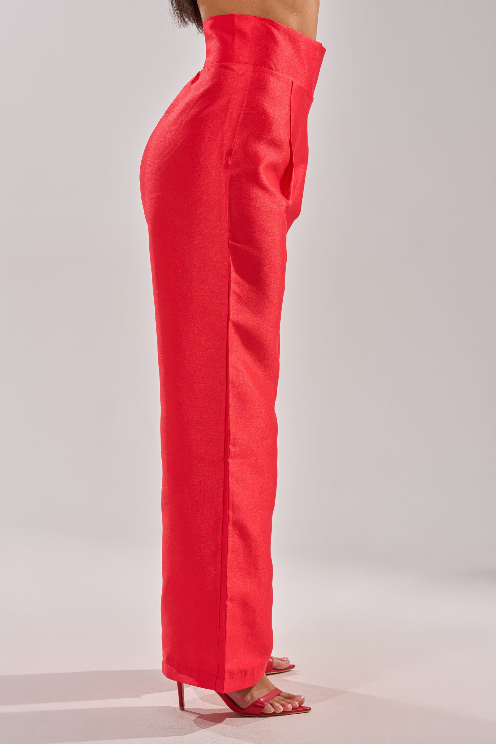 A woman stands sideways against a plain light background, wearing the BY MY SIDE TROUSER in bright red paired with matching red high-heeled sandals. 3