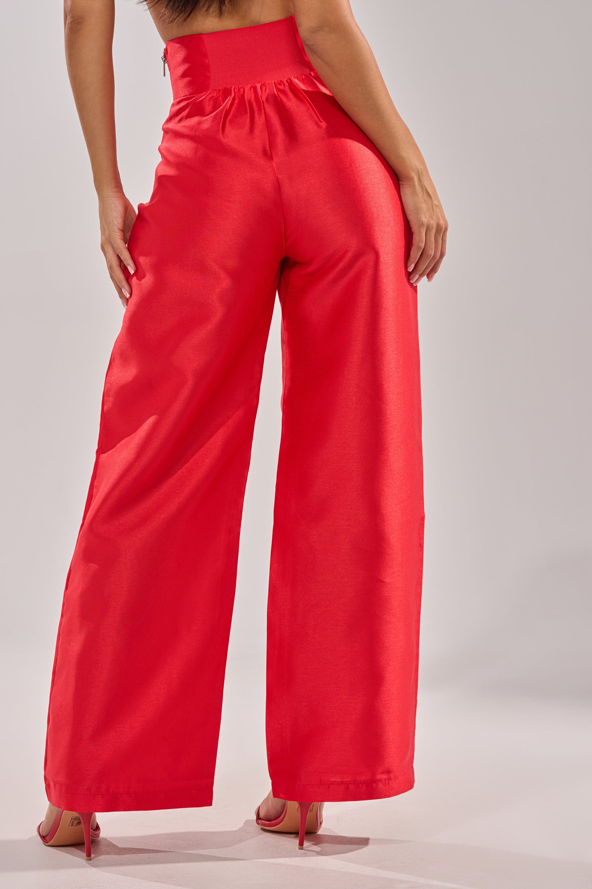 A person faces away, wearing BY MY SIDE TROUSER high-rise wide-leg pants and matching red heels. The bold, flowy trousers stand out against the light gray background, with their top half hidden from view. 4