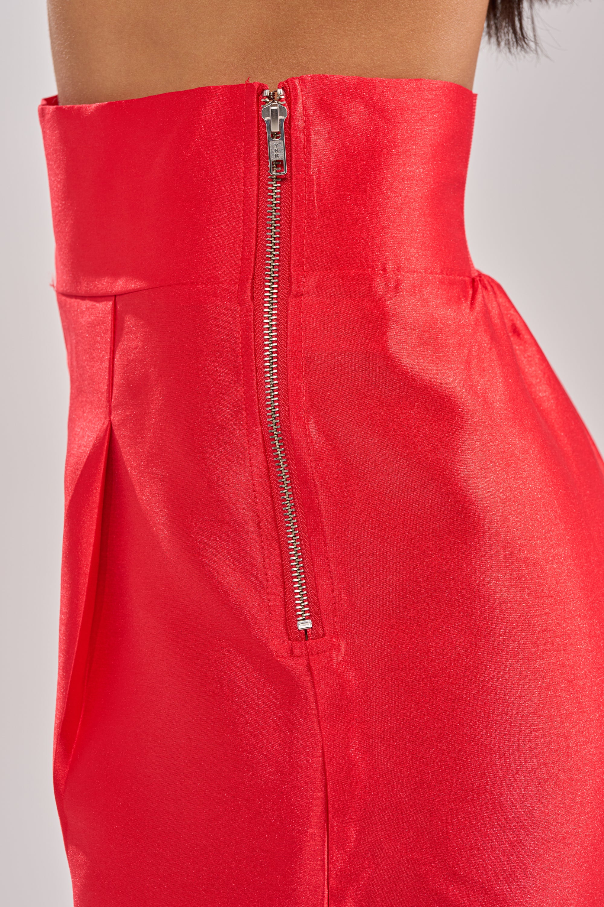 Close-up of a person wearing the BY MY SIDE TROUSER in shiny red satin with a silver side zipper. The smooth, high-waisted design adds an elegant touch to these bold statement trousers. 8