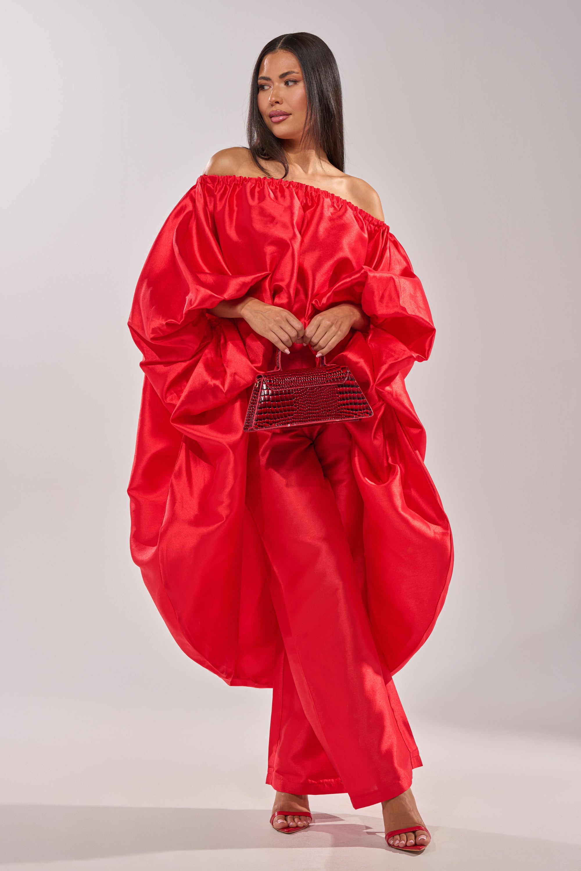A woman with long straight hair models the BY MY SIDE HIGH LOW BLOUSE in bold red, paired with matching pants and red heels. She holds a textured red handbag, standing against a plain light background. 5