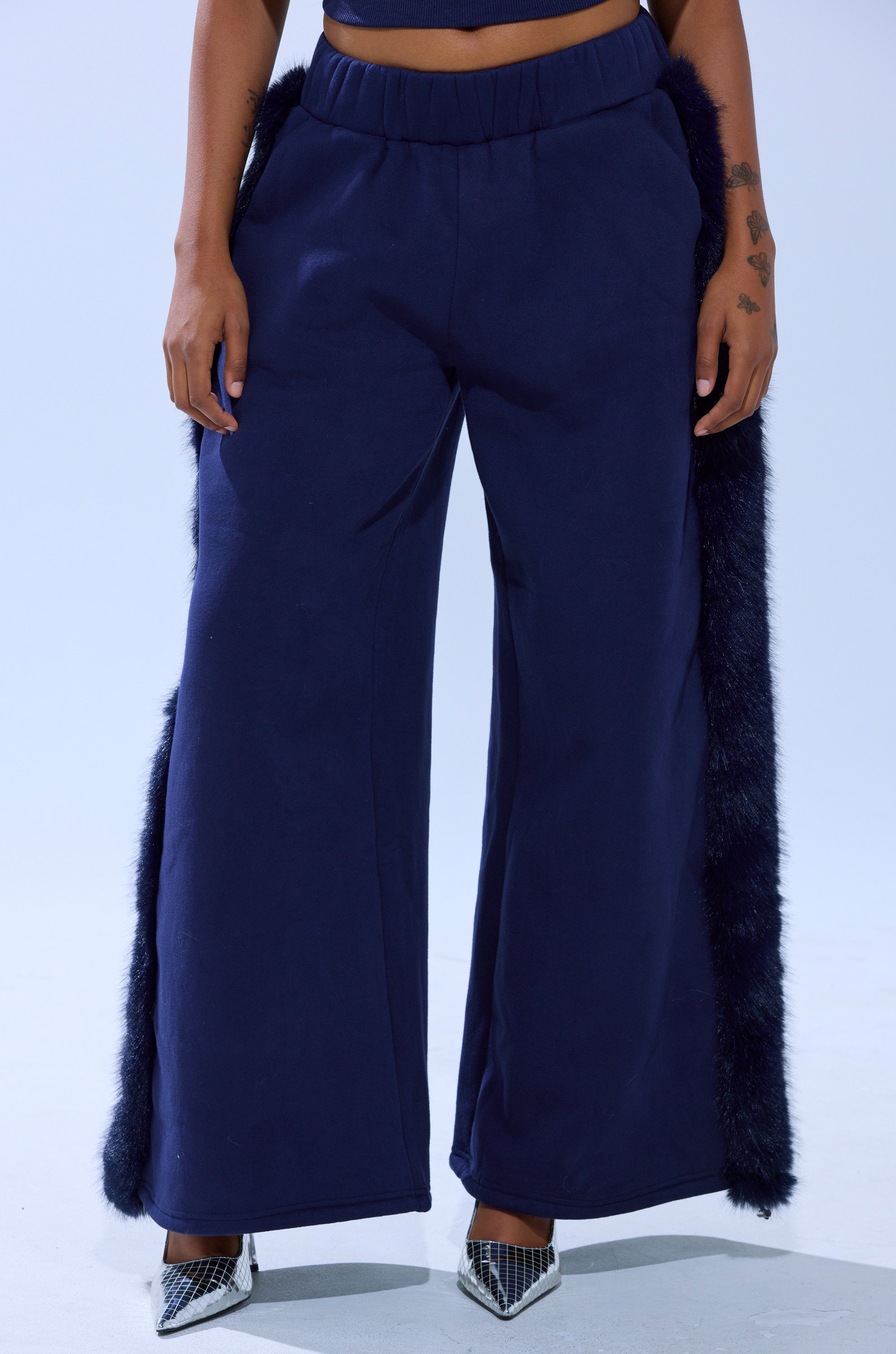 A person wearing the LUXE FUR JOGGER IN NAVY with faux fur side trim and metallic pointed-toe heels, standing against a light background.