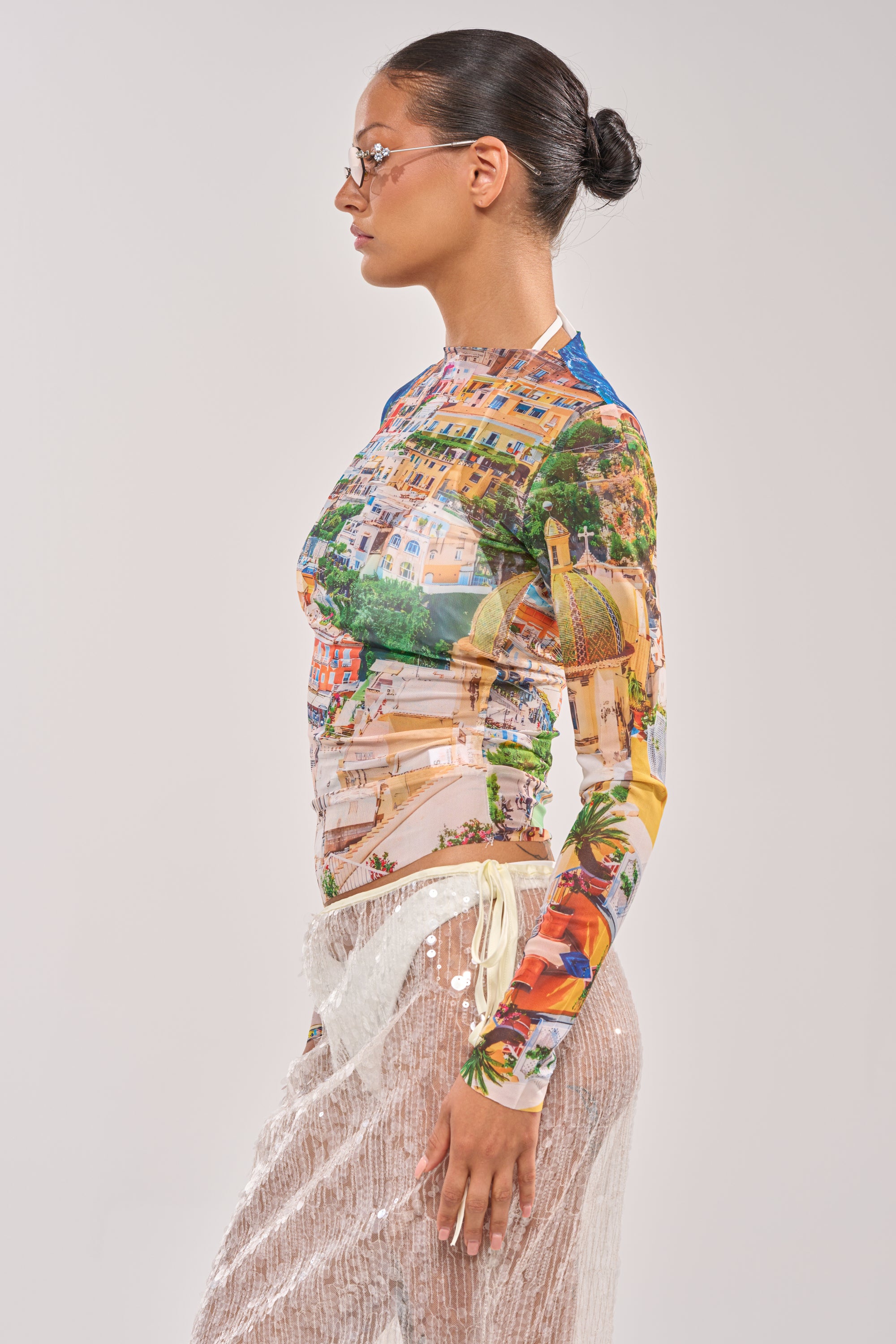 A woman with glasses and slicked-back hair stands in profile, wearing the AMALFI DAYS MESH TOP and sheer, sequined pants over beige shorts, against a plain light background. 4