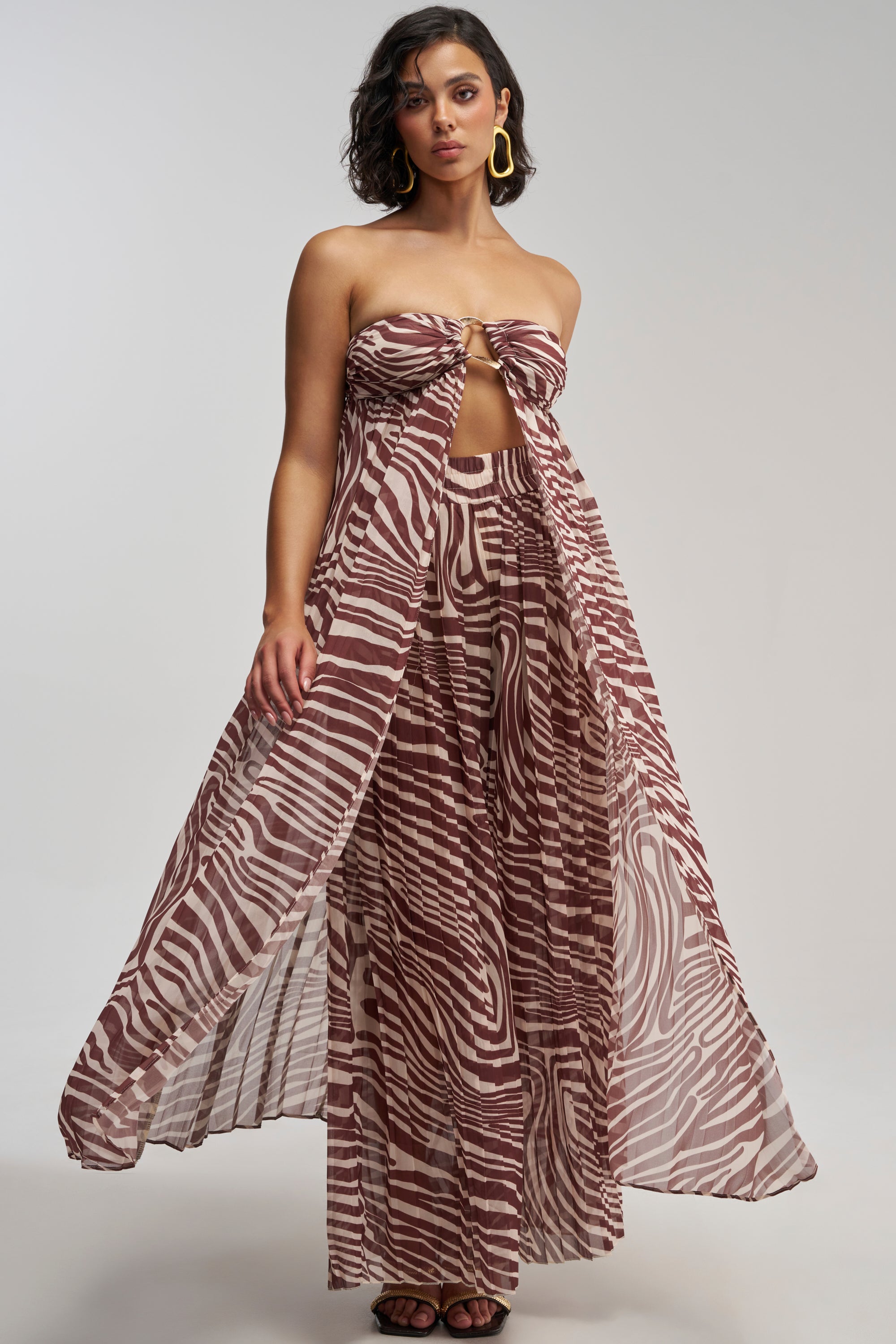 Woman wearing the DREAMING OF A VACA BLOUSE—a strapless, brown and white patterned sheer mesh top—paired with a flowing, sheer maxi skirt and matching wide-legged pants, standing against a plain background.