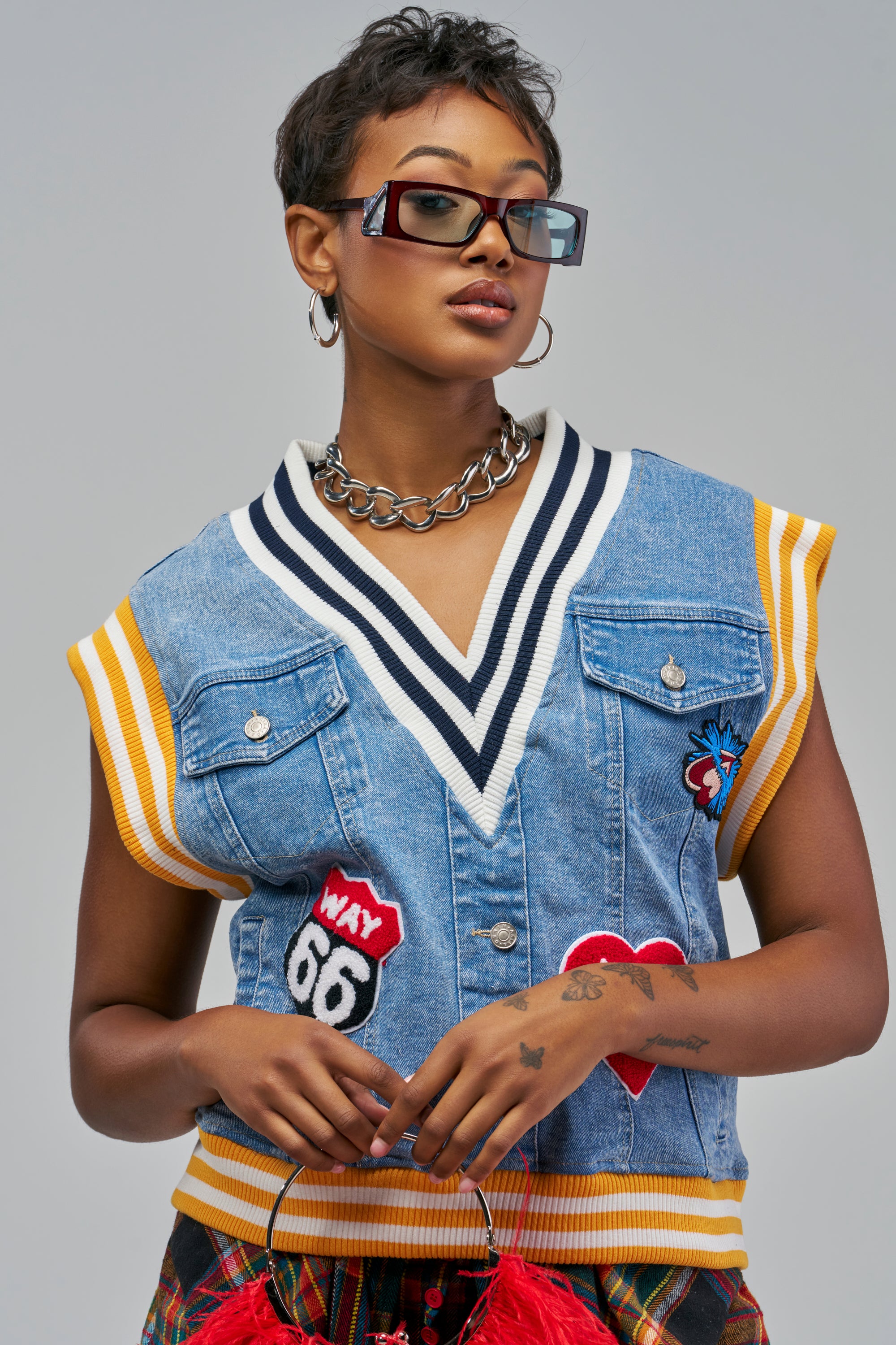 A light blue denim REAL LOVERS CLUB DENIM TOP with a V-neck, varsity-inspired striped ribbed trim, and heart and Route 66 embroidered patches, worn with rectangular sunglasses and a chain-link necklace.