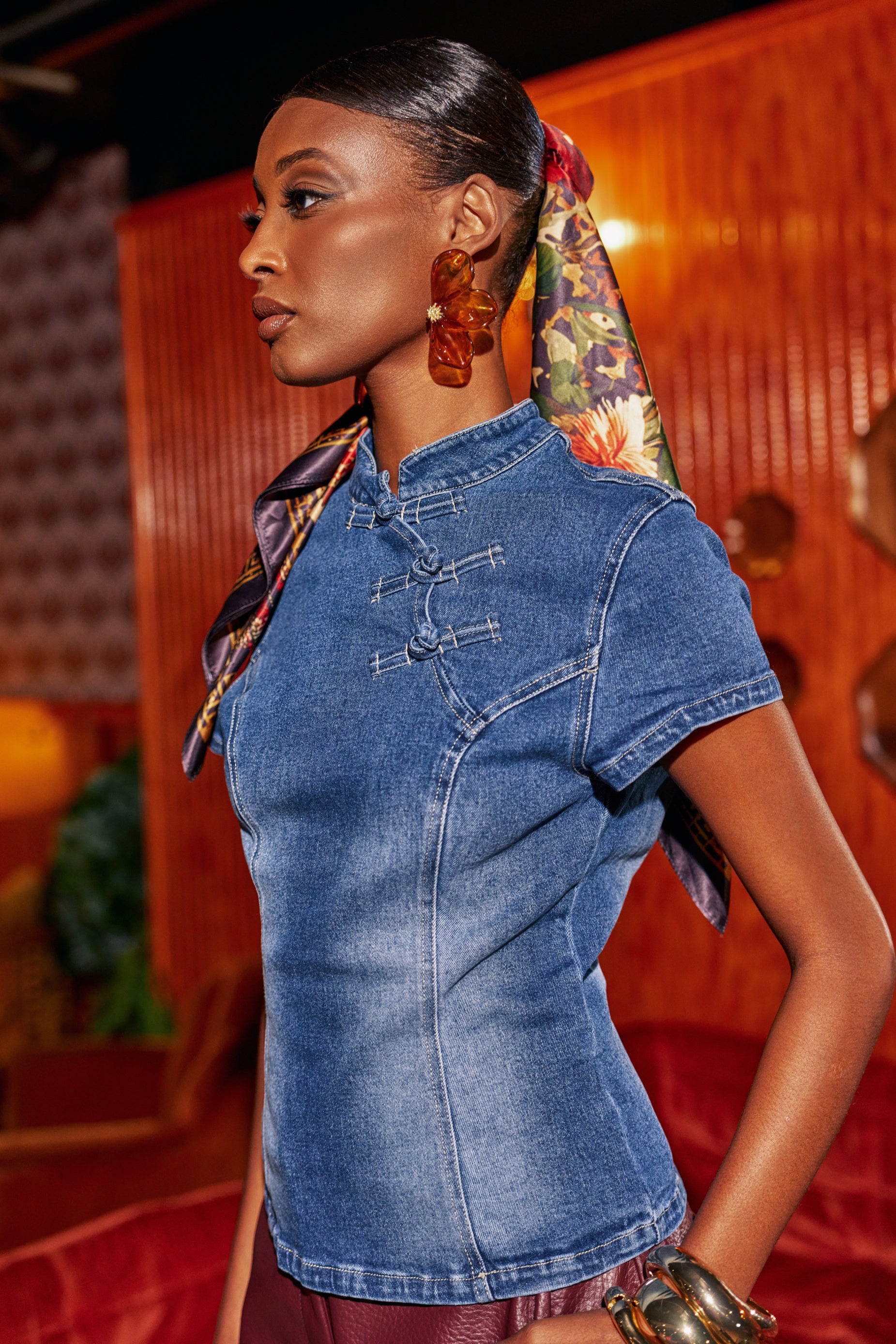 A person wears a DENIM DOLL FITTED TOP, a medium blue denim blouse with a mandarin collar and toggle button closures.