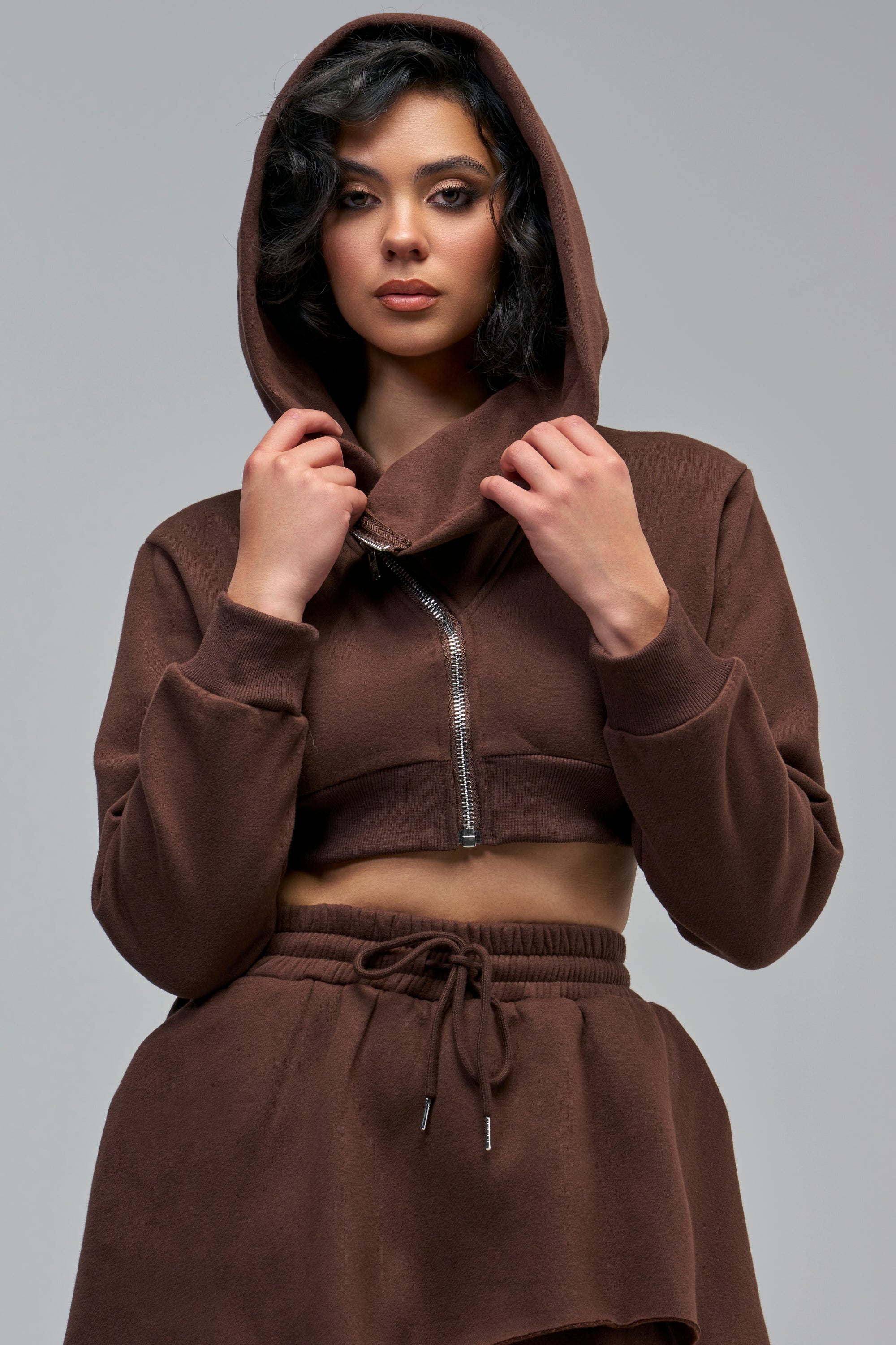 A woman wearing a brown MISS INDEPENDENT CROPPED HOODIE with an edgy high neck and a silver front zipper.