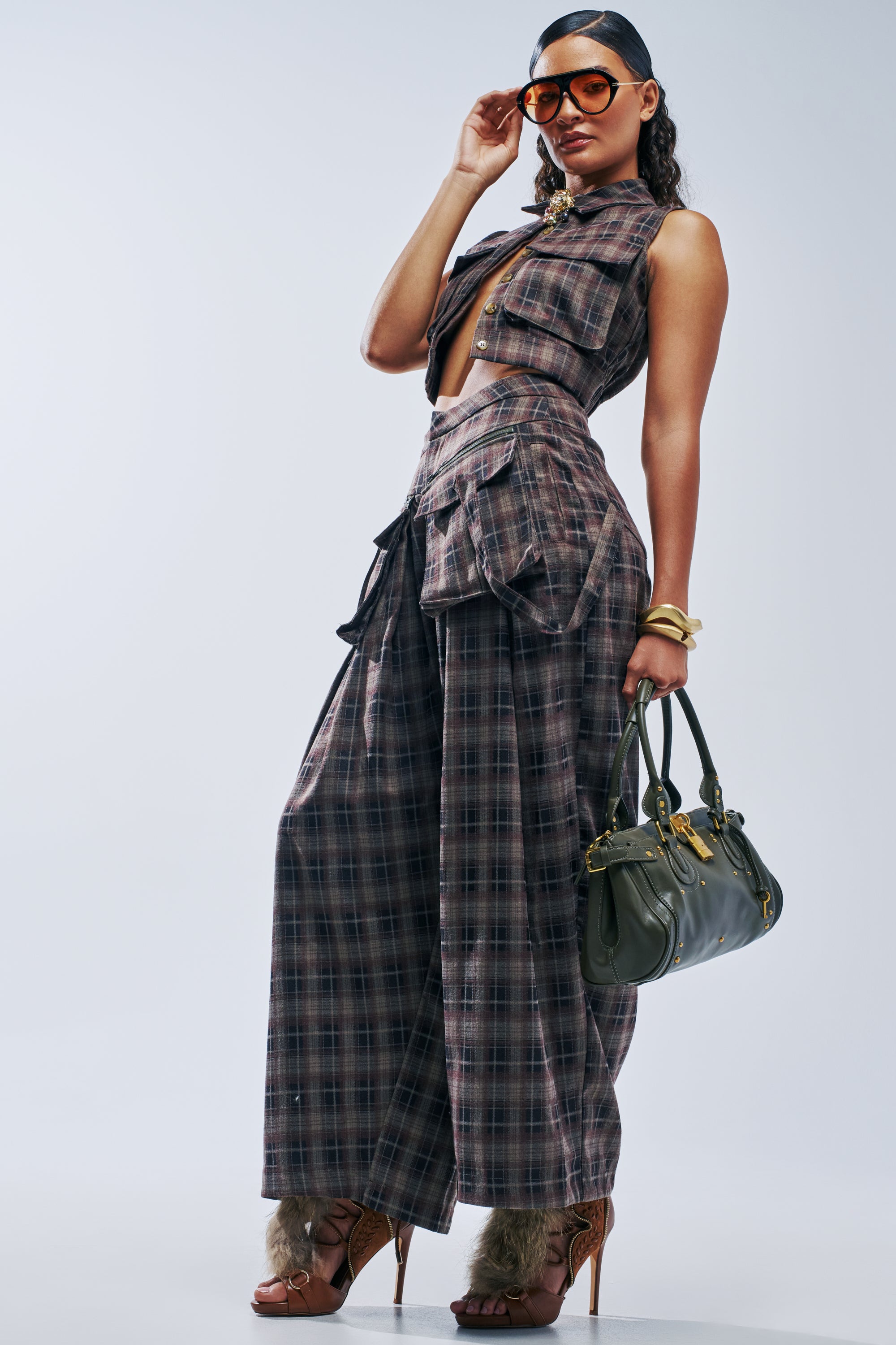 A person wearing a plaid sleeveless crop top and matching PLAID PRINCESS CARGO TROUSER with large side pockets, carrying an olive green handbag.