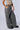 A person wearing a cropped beige top and high-waisted, wide-leg DONT STOP MOVIN TROUSER by AKIRA with their hands in the pockets. The jeans have a vintage look, and the individual is also wearing black platform shoes. The background is plain and neutral.