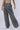 The image shows a person from behind wearing the AKIRA DONT STOP MOVIN TROUSER, which are high-waisted, wide-leg, mineral wash denim trousers with two back pockets. The person is also wearing a light-colored, slightly cropped top. The background is plain and light-colored.