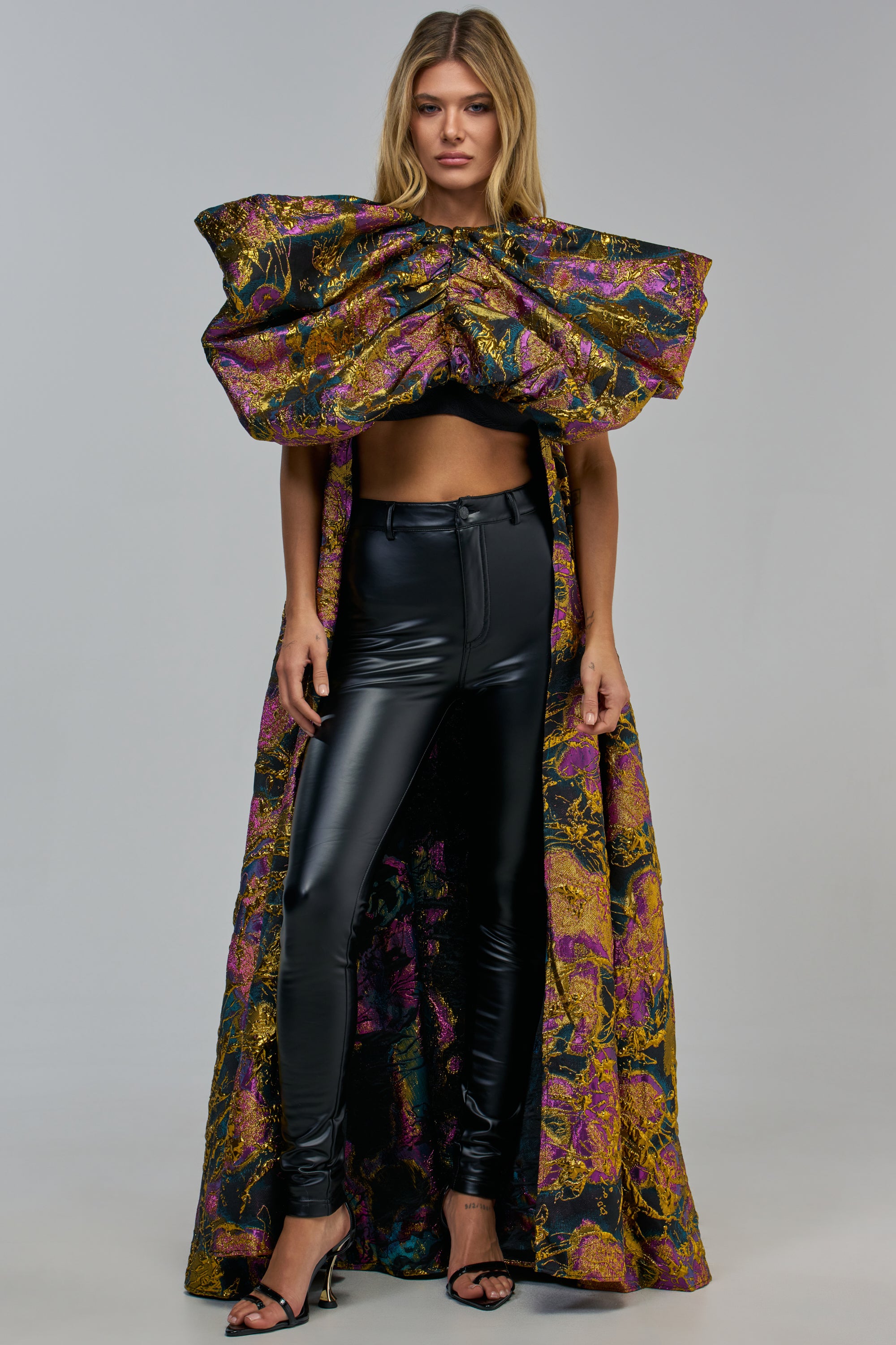 A person wears black faux-leather pants and a MIDNIGHT BLOOM STATEMENT BROCADE TOP with oversized, puffed sleeves and a metallic purple and gold floral pattern.