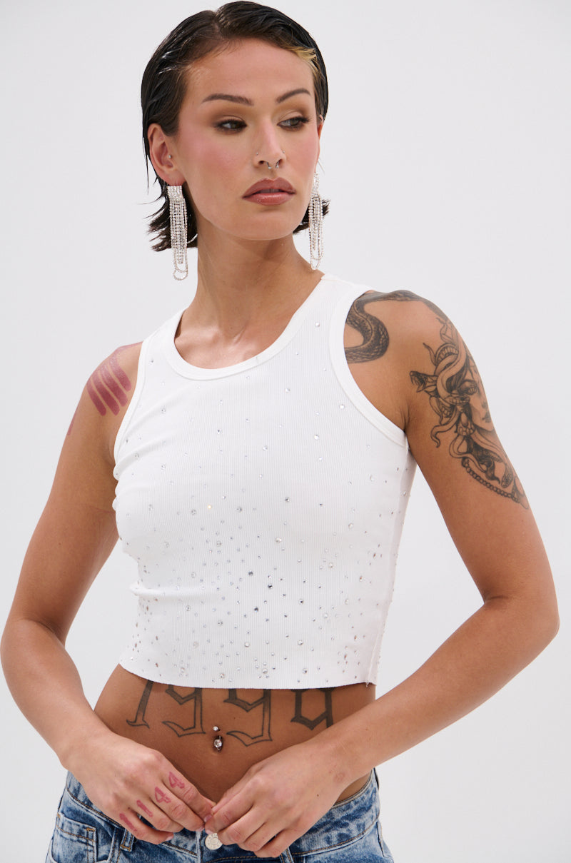 A person with wet, slicked-back hair models the RHINESTONE QUEEN TANK in Y2K style, paired with blue jeans and long dangling earrings. Tattoos are visible on their arm, shoulder, and stomach as they look to the side with a neutral expression. 0