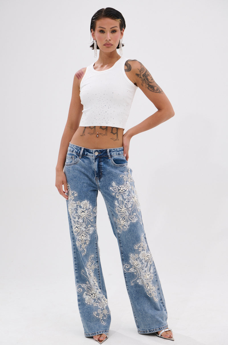 A person with short dark hair and tattoos confidently poses in the RHINESTONE QUEEN TANK and high-waisted blue jeans with white floral embroidery, channeling effortless Y2K vibes against a plain white background. 5