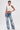 A person with short dark hair and tattoos confidently poses in the RHINESTONE QUEEN TANK and high-waisted blue jeans with white floral embroidery, channeling effortless Y2K vibes against a plain white background.