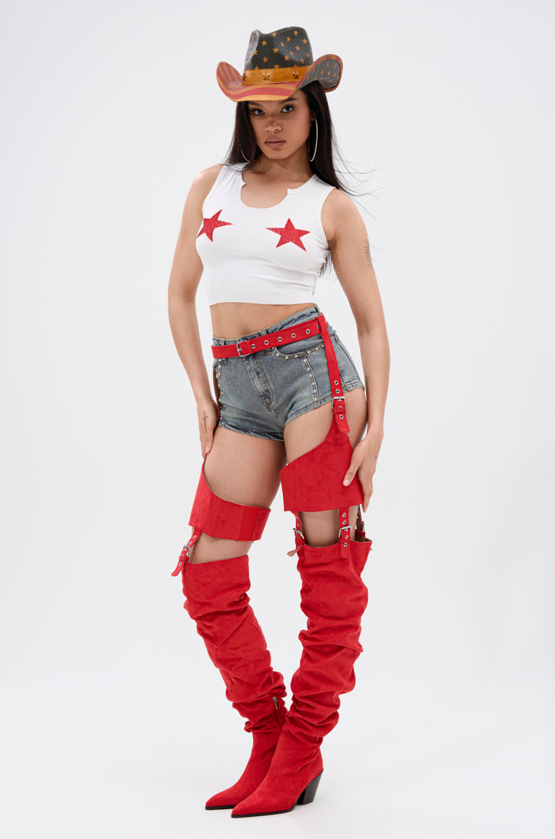 Woman in a cowboy hat, SEEING STARS CROPPED TANK TOP with glitter star appliqués, denim shorts, red belt, and tall red boots poses confidently against a plain white background.