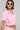 A person in white cat-eye sunglasses flaunts their chic style in the WORK FOR IT Mineral Washed Cropped Button Down in Pink, featuring short sleeves and front pockets. They accessorize with a pearl necklace and large hoop earrings, while their dark bob-styled hair complements the edgy tattoo on their midriff.