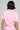 A person with short, dark hair is facing away, wearing a light pink WORK FOR IT Mineral Washed Cropped Button Down and matching pants. The background is gray and unobtrusive.