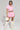 A person wearing the chic WORK FOR IT Mineral Washed Cropped Button Down in pink from the AKIRA Label, paired with a matching mini skirt, white fuzzy boots, and sunglasses. They are holding a fluffy white handbag, exuding a modern and stylish vibe.