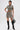 A woman with tattoos and slicked-back hair poses against a white background wearing the VENOM CROPPED LEATHER BUTTON DOWN in gray snakeskin, a matching mini skirt, black knee-high boots, and holding a black handbag.