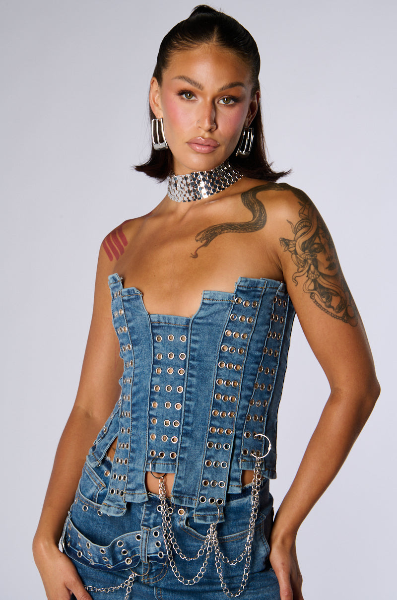 A person wearing the JUST WANNA ROCK DENIM TUBE TOP, paired with matching denim pants. They have visible tattoos on one arm and shoulder and are accessorized with a silver choker and large hoop earrings. They are standing against a plain background.