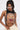 A woman with long dark hair in pigtails wears angular sunglasses and the RAWR TANK—a racerback crop top with a roaring tiger face print and silver chain side details—paired with cream pants. She gazes slightly down and to the side.