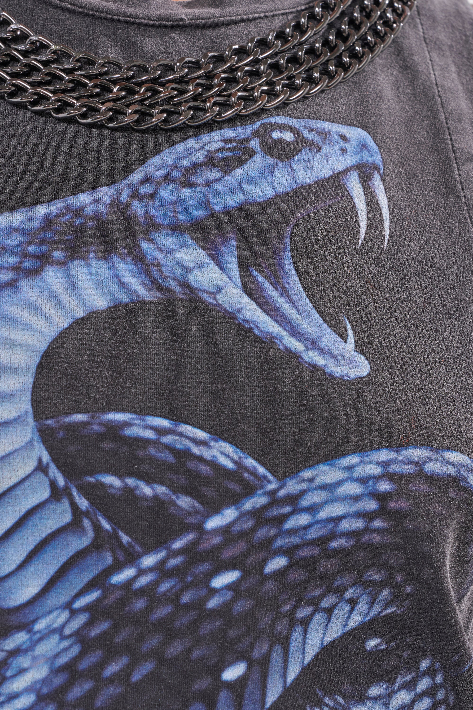 Close-up of the HISS HISS CHAIN DETAIL TANK, featuring a bold blue snake graphic with open mouth and fangs, paired with a metal chain-link necklace resting on the collar. 7