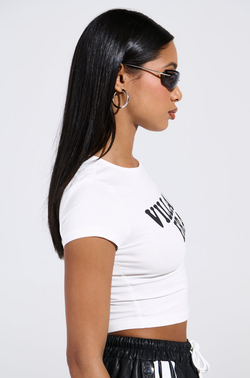 A person with long black hair is wearing a stretchy cotton VILLAIN ERA TEE, black pants with white drawstrings, accessorized with oval sunglasses and large hoop earrings. They are standing against a plain background in a cropped silhouette.