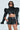 Wearing a futuristic ensemble, someone sports the ultra-cropped Keep It Coming Top with a shiny black look and structured, exaggerated shoulders, paired with matching high-waisted shorts. They complete the look with long hair and dark sunglasses.