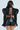 A rear view of a person with long brown hair in the KEEP IT COMING TOP, featuring shiny black leather, structured shoulders, and a lace-up open back. Paired with high-waisted black leather shorts, this chic outfit stands out against the plain white background.