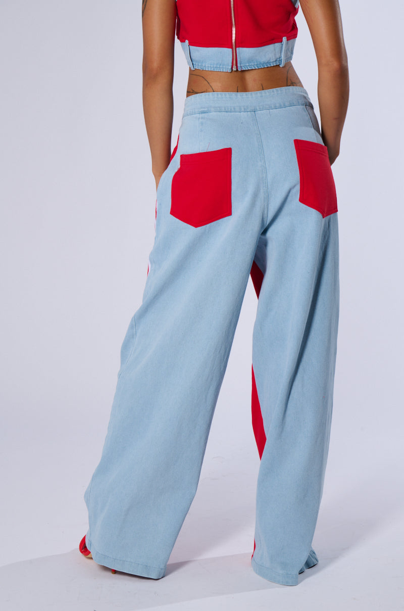 A person stands facing away from the camera, wearing sporty chic style light blue wide-leg HEADS UP FLARE PANTS with large red back pockets. They are paired with a red crop top featuring a zipper on the back, revealing a hint of midriff. The background is plain white.