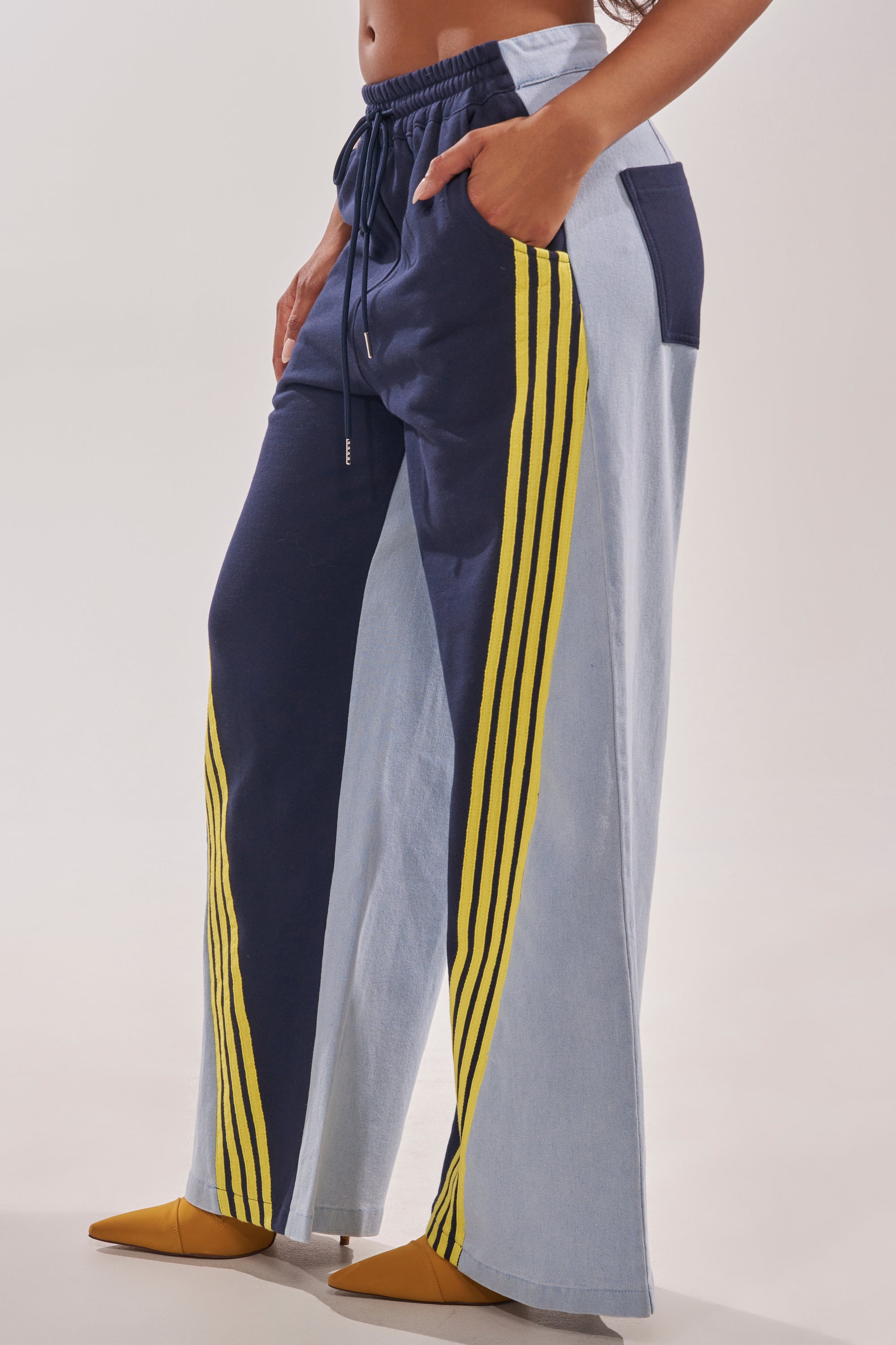 Wearing the HEADS UP DENIM WIDE LEG JOGGER IN NAVY, featuring navy blue with yellow stripes on one leg and light-wash denim on the other, drawstring waist, pockets—styled with mustard yellow pointed-toe shoes. 3