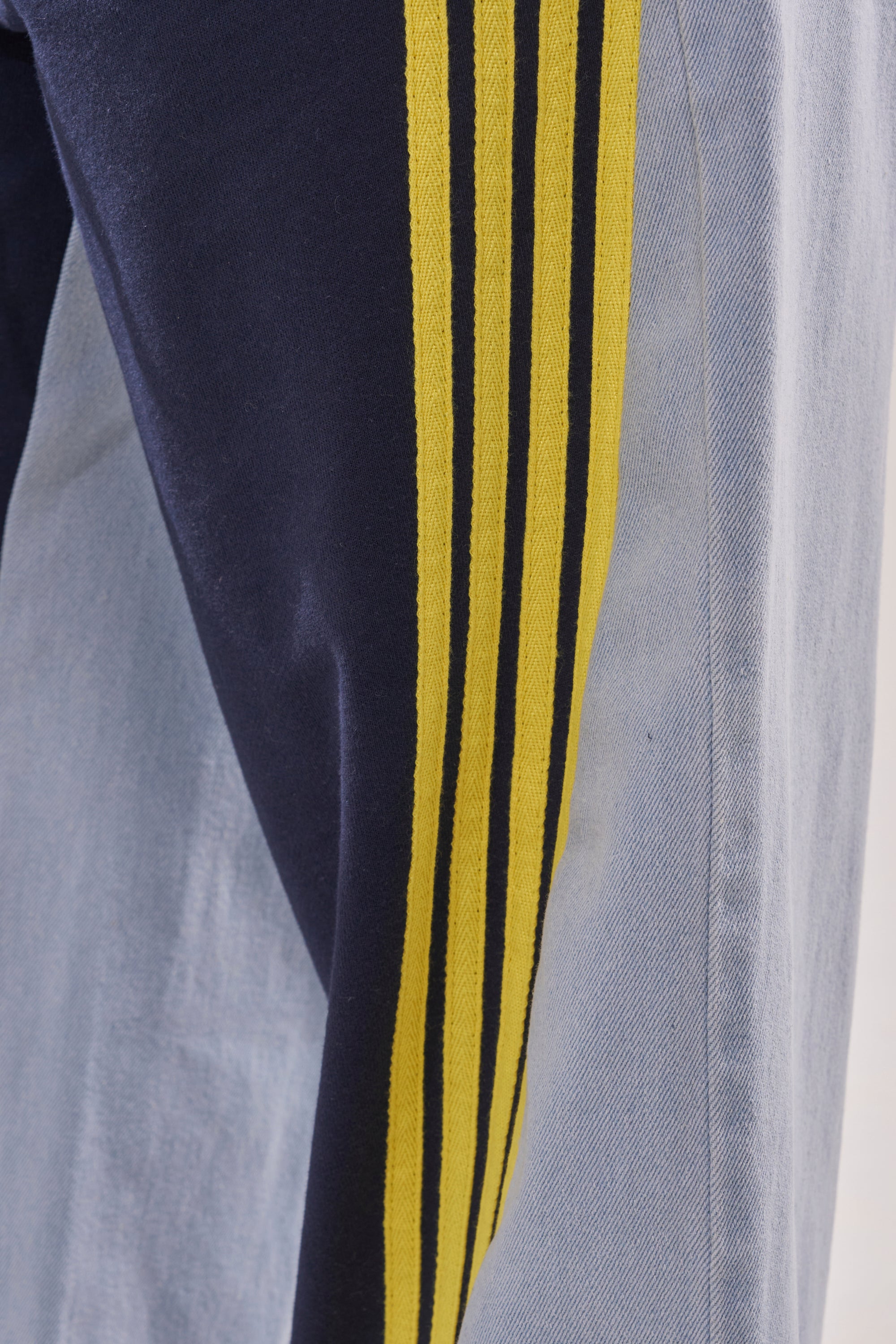 Close-up of the HEADS UP DENIM WIDE LEG JOGGER IN NAVY, showcasing dark blue fabric with three yellow stripes beside light blue denim. Visible textures and seams enhance its sporty style. 7