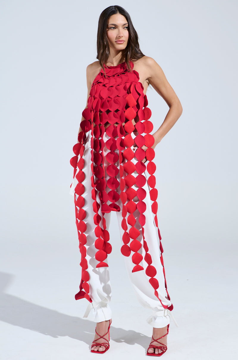 A woman poses in the Lights Flashing Halter Tie Neck Top in red, styled with red heeled sandals and featuring a tie-neck halter design. She has long, dark hair.