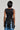 Rear view of a person with shoulder-length dark hair wearing the LIGHTS FLASHING TOP, which features a bodycon fit and layered circular patterns cascading down the back. They pair it stylishly with light blue jeans for a chic look.