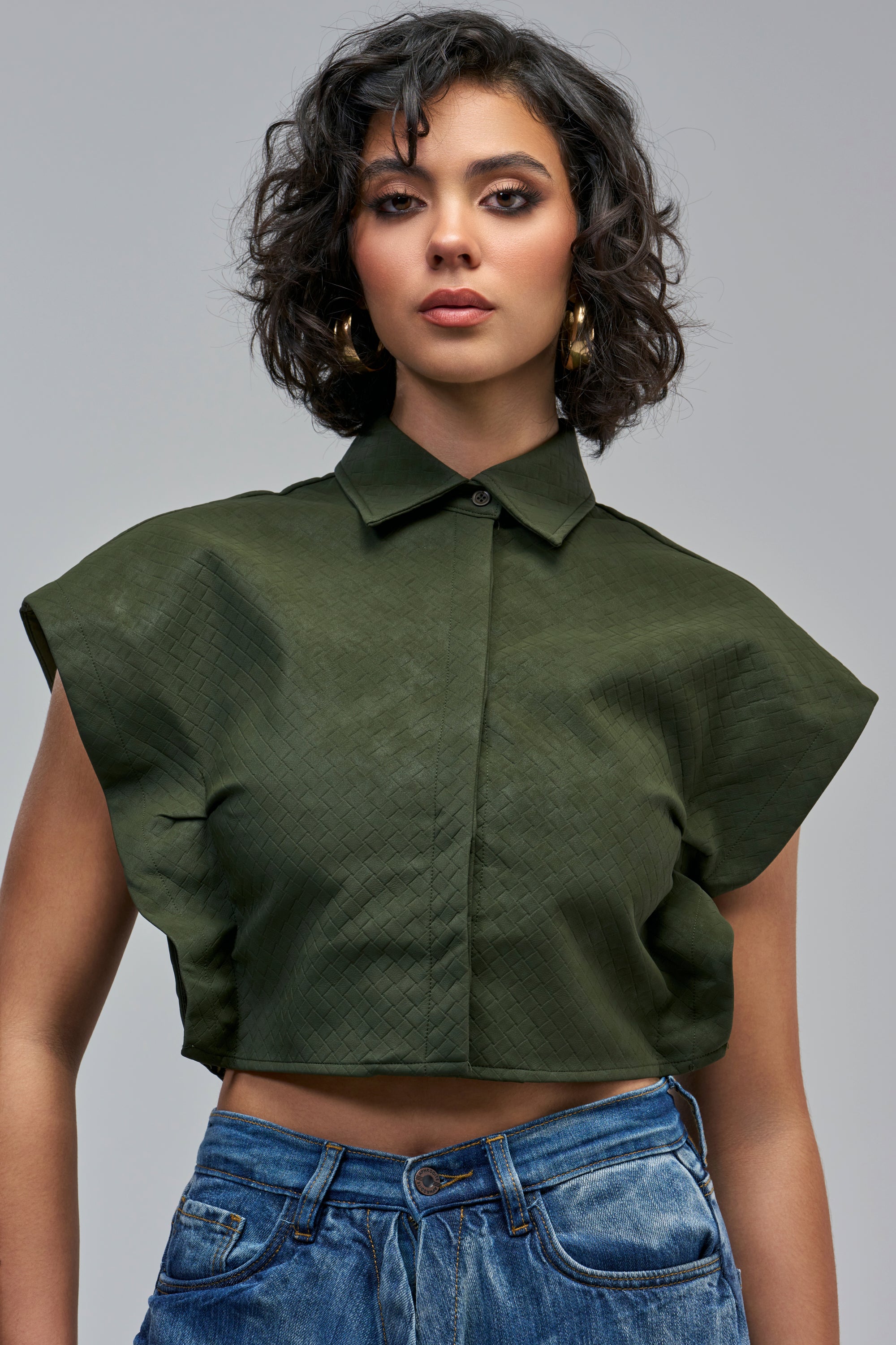 LUXE LIFE SUEDE CROPPED BUTTON DOWN in olive green with a woven texture, short cap sleeves, and a subtle grid pattern, worn with blue jeans.