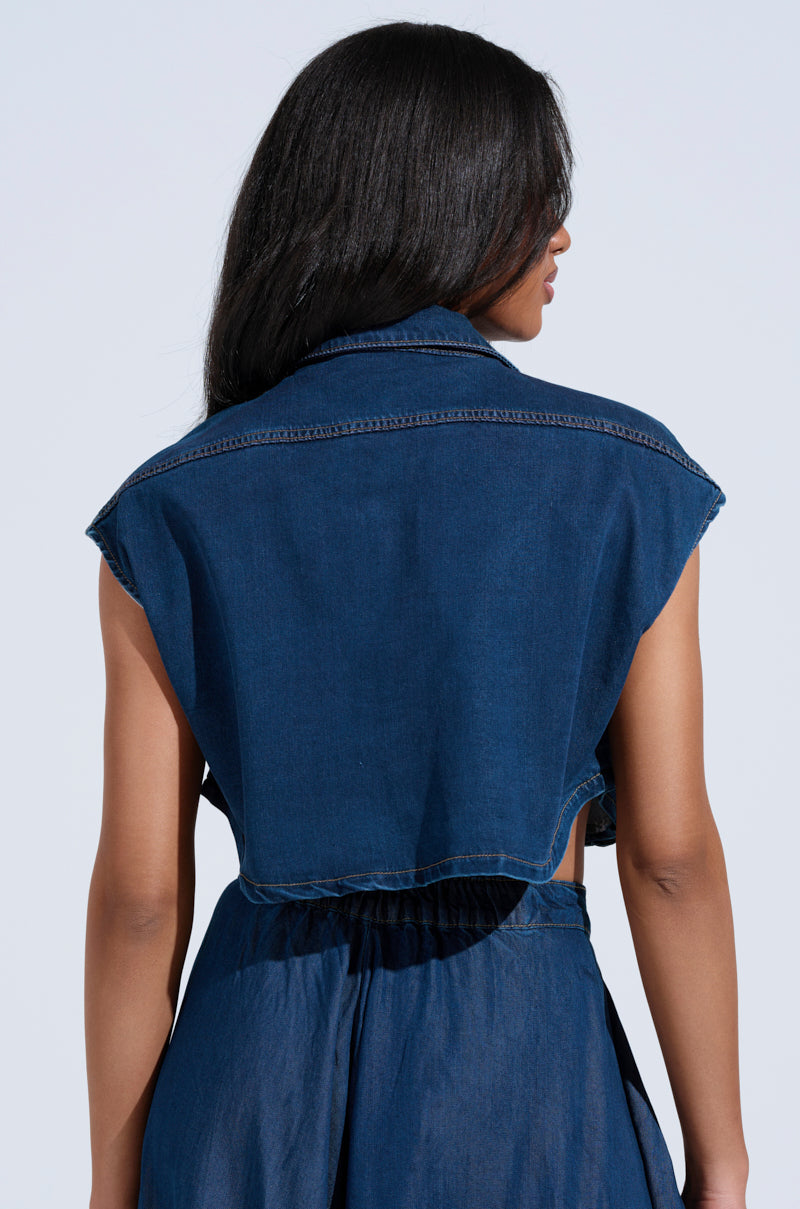 The image features a person with long dark hair from the back, highlighting the cropped silhouette of a sleeveless "CARRIE BUTTON DOWN DENIM VEST TOP" paired with matching high-waisted pants against a plain light gray background.