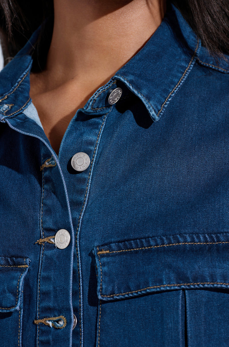 Close-up of a person wearing the CARRIE BUTTON DOWN DENIM VEST TOP in dark blue. The visible stitching and silver buttons enhance its casual style, while the sleeveless design adds a modern touch to its classic denim look, with pockets completing the ensemble.