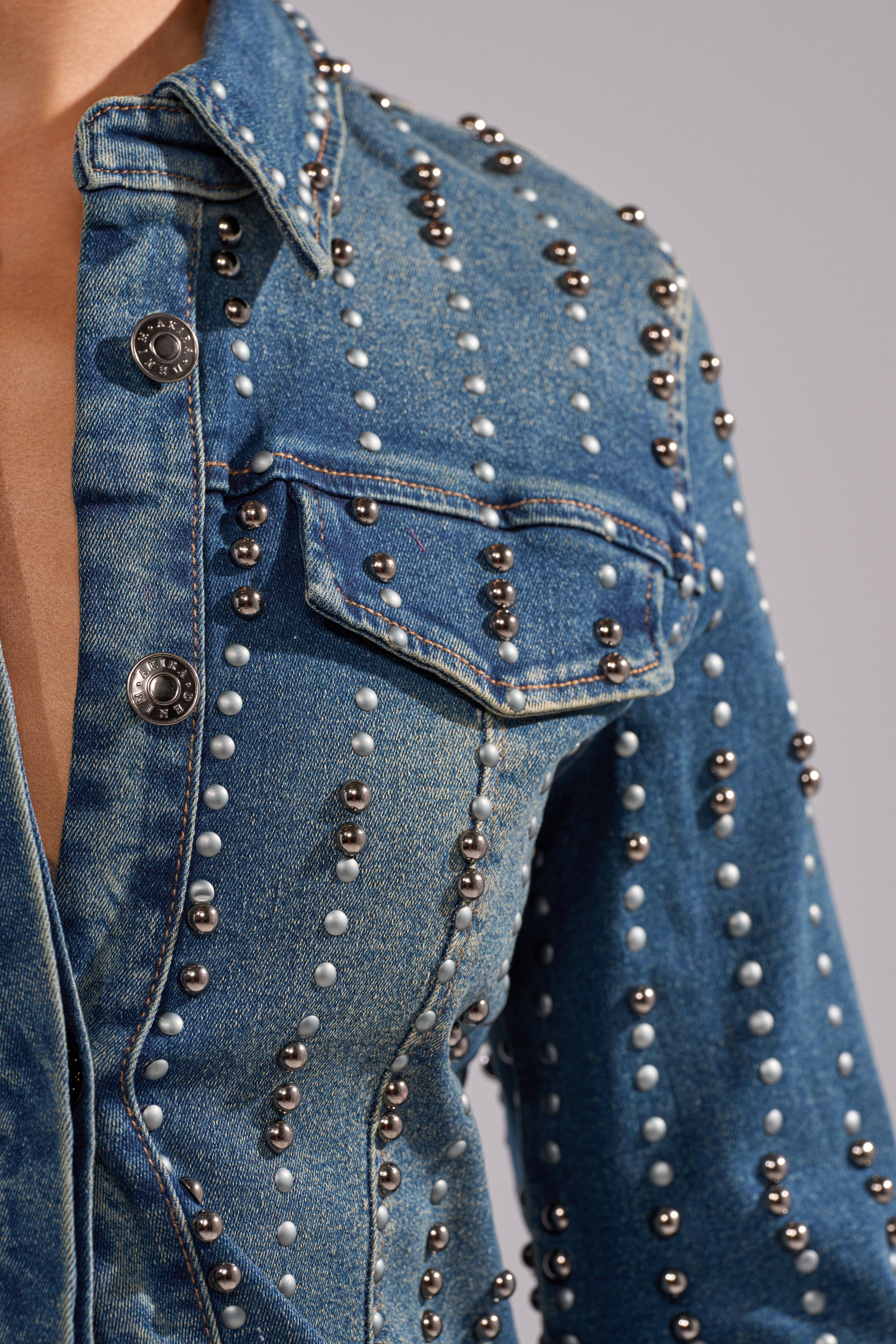 Close-up of the GLAMOUR STUDDED BUTTON DOWN DENIM TOP in blue, detailed with silver and white round studs in vertical lines, a visible chest pocket, and metal buttons.