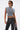 A person confidently stands against a plain white background wearing the ABLE TO SEE ME STRAPPY TOP, featuring a deconstructed corset-inspired gray design with hanging straps, paired with grommet-detailed black pants, sunglasses, and a black bag.