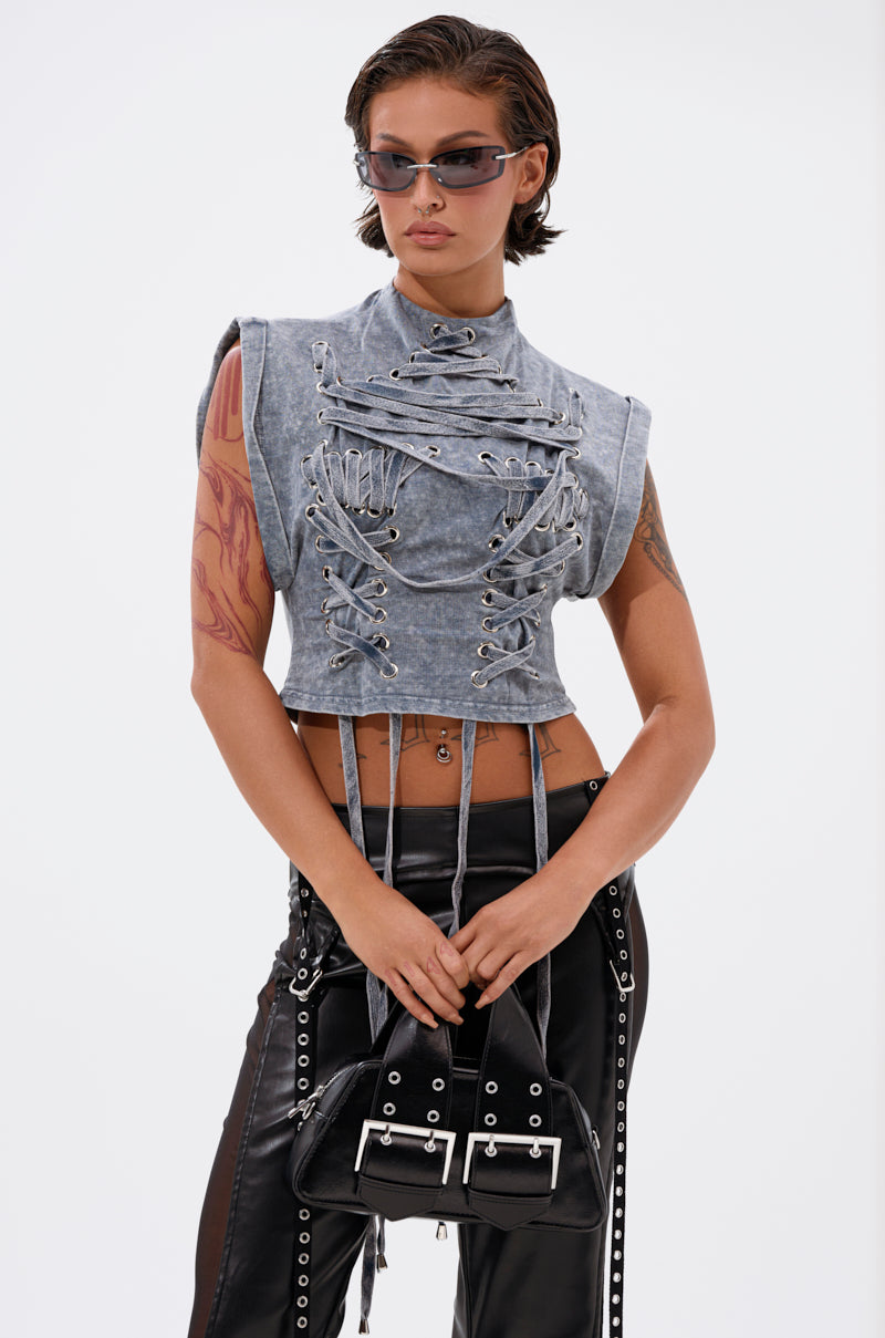 Wearing the ABLE TO SEE ME STRAPPY TOP, a person with short, dark hair and sunglasses styles it with black faux leather pants featuring grommets and a black handbag with silver buckles against a plain white background. 1