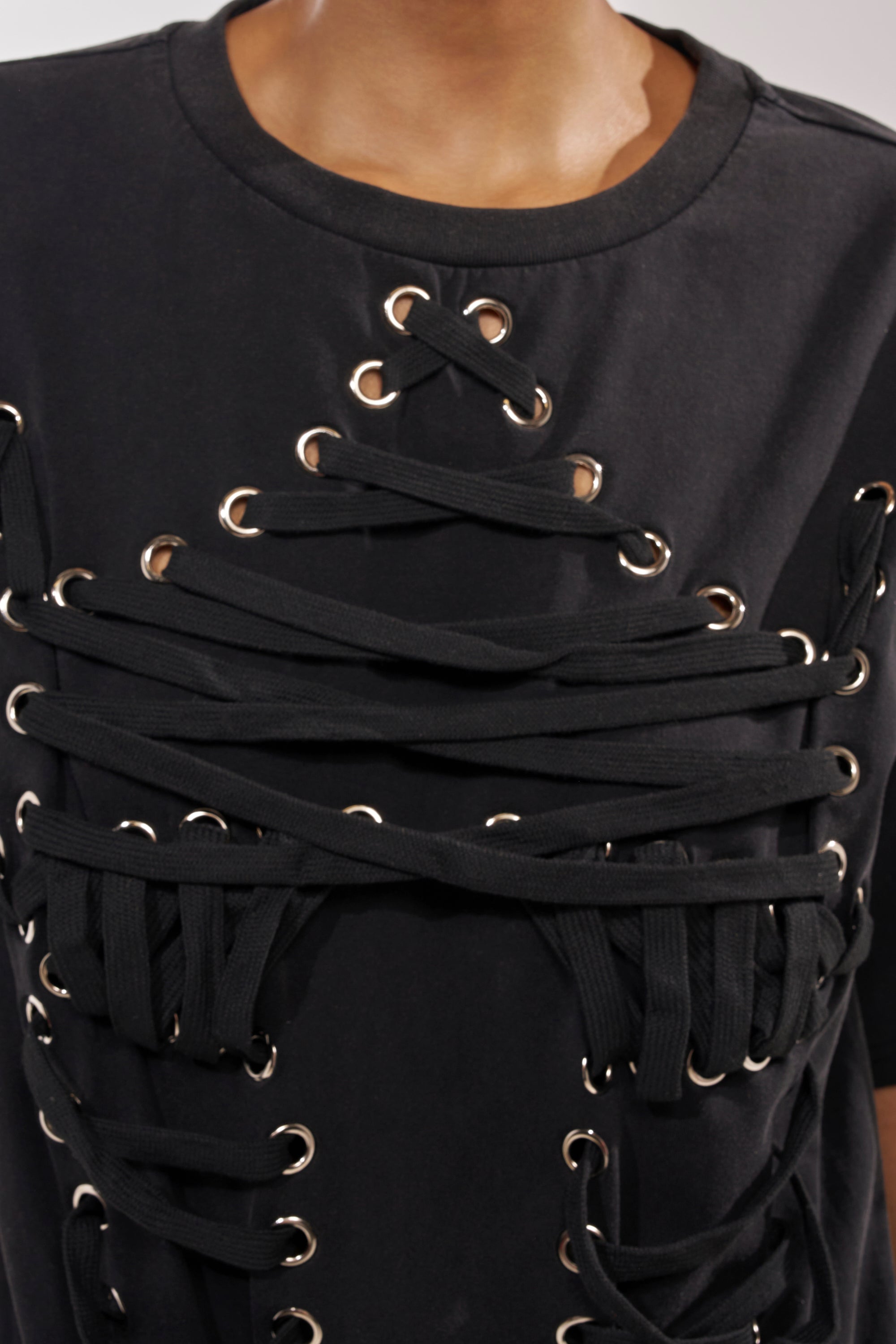 Close-up of a person wearing the LACED UP MINERAL WASH T-SHIRT, a black graphic tee featuring crisscrossed black laces through silver eyelets across the chest—a bold option for concert outfits. 6