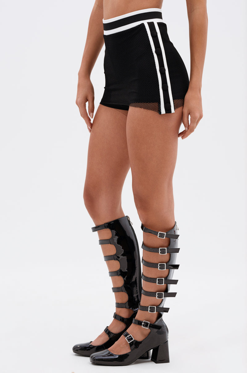 Against a plain background, a person wears the CANT GET ENOUGH MESH MINI SKIRT paired with black knee-high, open-toe boots featuring multiple straps and chunky heels. 3