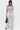 A woman stands against a white background wearing the SET YOU FREE PALAZZO PANT and a matching off-the-shoulder crop top with a black and white abstract print, styled with a black handbag and black heeled sandals.