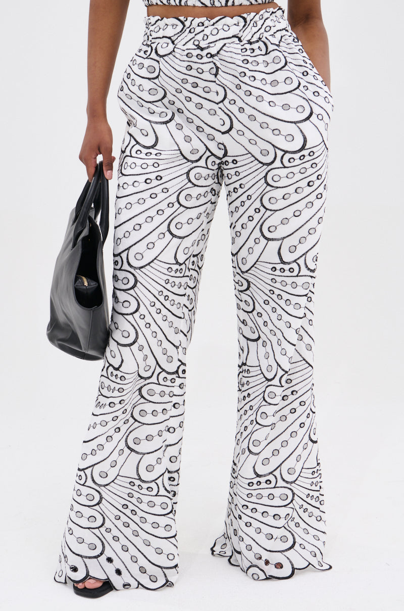 A person wearing the SET YOU FREE PALAZZO PANT featuring a high rise, wide-leg fit and black and white abstract pattern stands holding a black handbag; their face is not visible.
