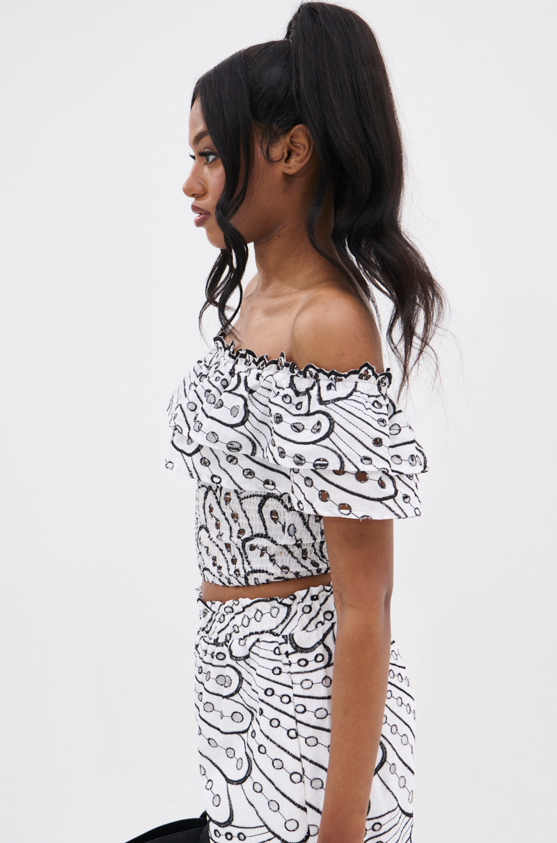 A woman with long, wavy black hair in a high ponytail models the SET YOU FREE OFF THE SHOULDER BLOUSE and matching skirt with an abstract stitched pattern, shown in profile against a plain white background for a cropped silhouette look.