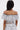 A woman with long dark hair stands with her back to the camera, wearing the SET YOU FREE OFF THE SHOULDER BLOUSE and matching skirt in an abstract stitched pattern. A tattoo appears on her upper right back.