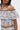 A woman models the SET YOU FREE OFF THE SHOULDER BLOUSE, showcasing its ruffled, cropped style with black and gray abstract stitching and matching high-waisted bottoms, her wavy hair styled as she stands against a plain white background.